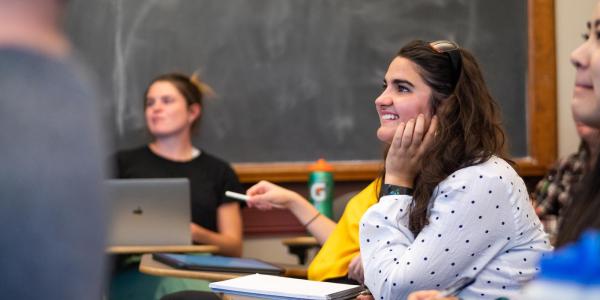 A student smiles while looking ahead at a lecture presentation