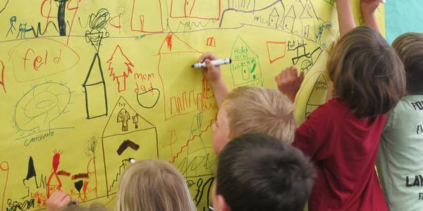 Children drawing with markers their vision of a town on paper pinned to the wall.