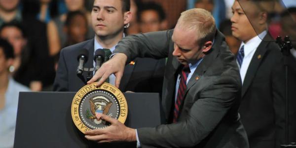 A person straightening a United States seal on a podium
