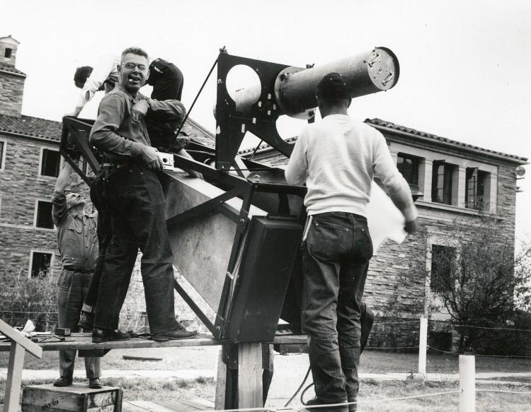 In a black and white photo, four men assemble a large telescope
