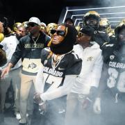 Artist Lil Wayne is surrounded by football players, Coach Prime, Chip and others. A slight mist floats in the air. (Photo by David Marckel/University of Colorado)