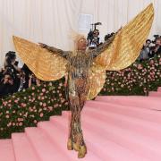 Bill Porter appears at the Met Gala in entirely gold beaded attire, including large wings extending beyond his hands. 